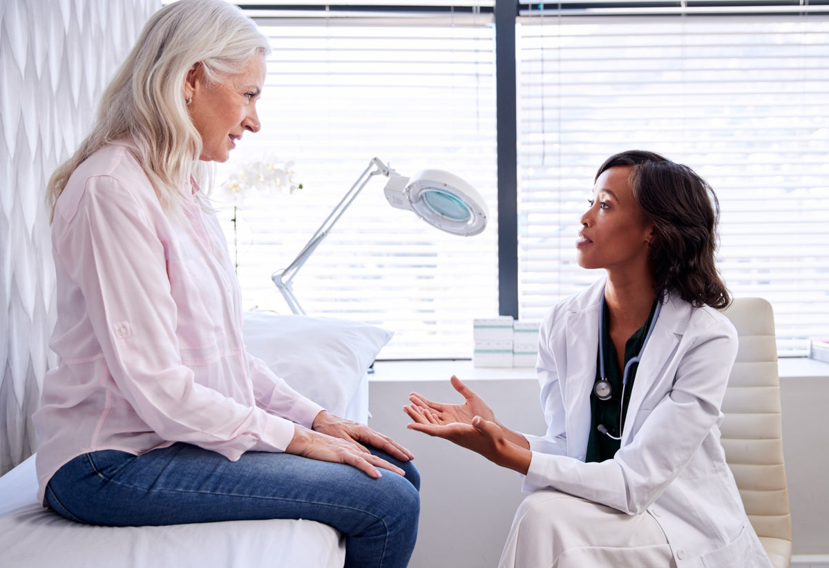 A woman speaking with a doctor in an examination room.